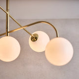 Close-up of Endon Sinclair semi-flush ceiling light showing three opal glass globes on brushed brass arms against a light grey background.
