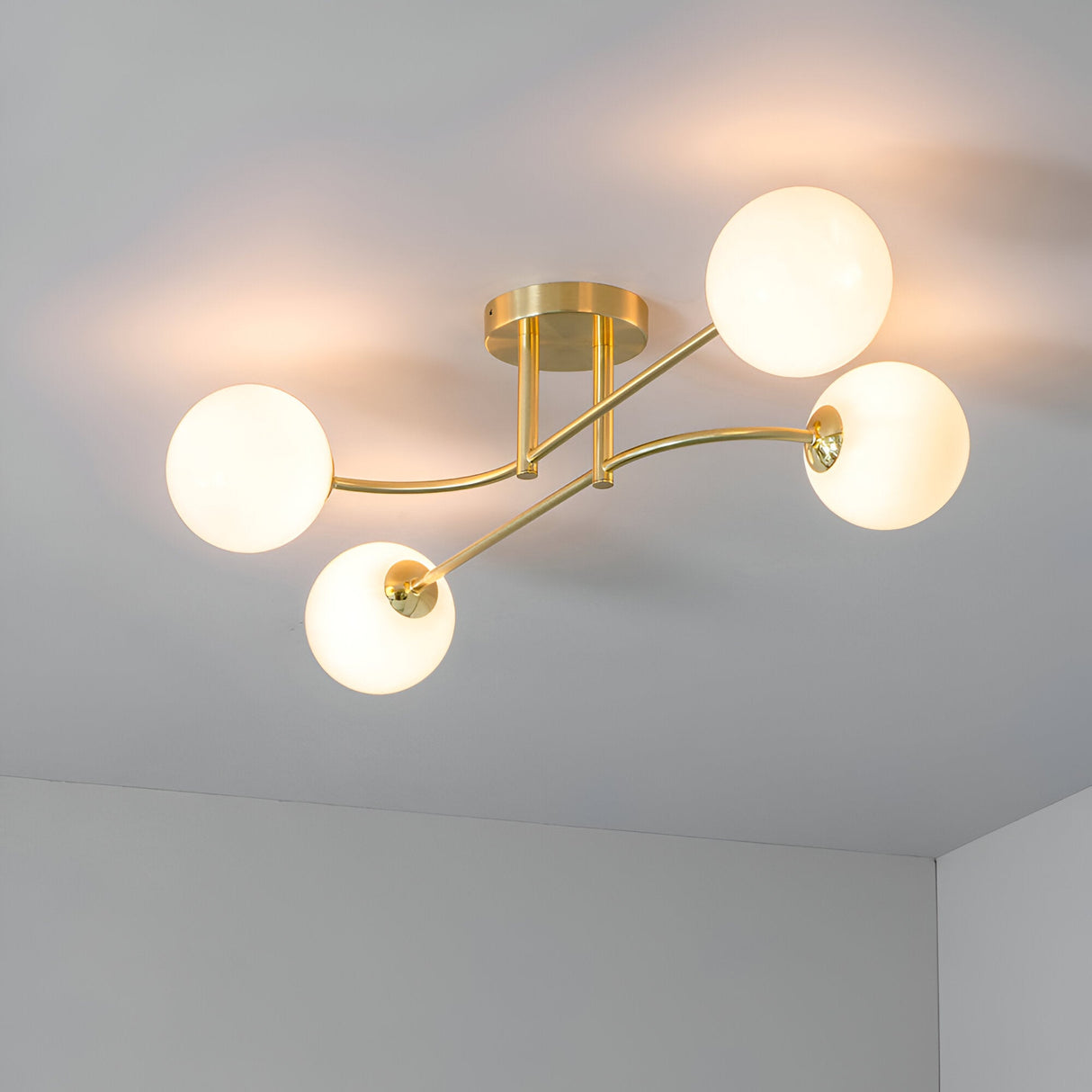 Endon Sinclair 4 light semi-flush ceiling light in brushed brass, with four curved arms holding opal glass globe shades on a white ceiling.