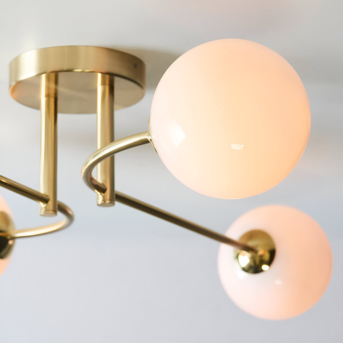 Close-up of Endon Sinclair semi-flush ceiling light in brushed brass, showing the circular ceiling plate and curved arms holding opal glass globe shades.