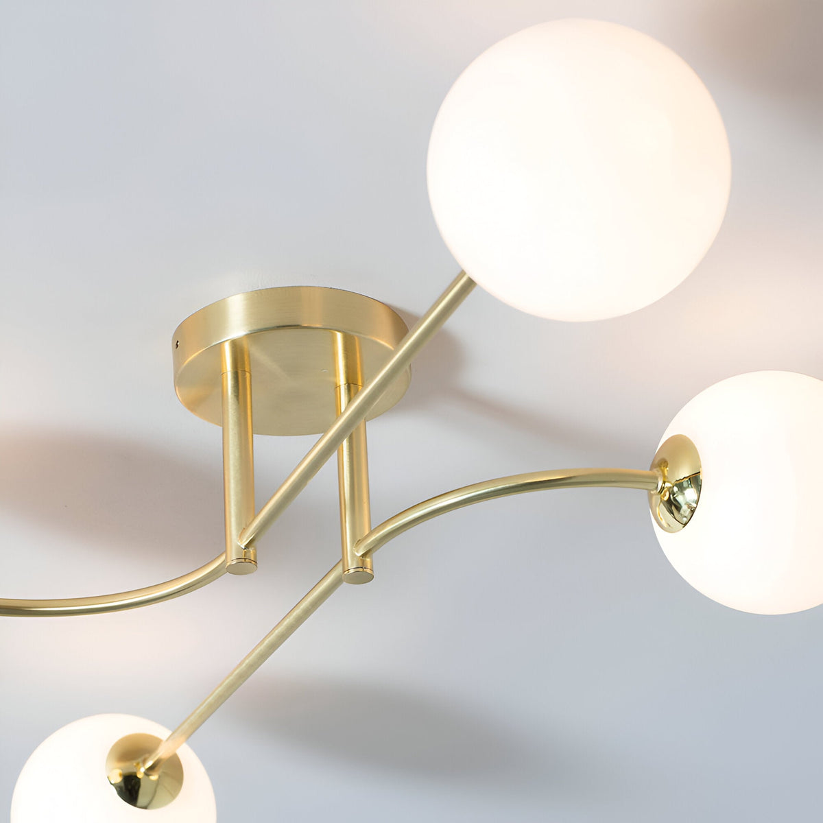 Endon Sinclair 4 light semi-flush ceiling light in brushed brass, viewed from below showing the central plate, curved arms and white glass globe shades.