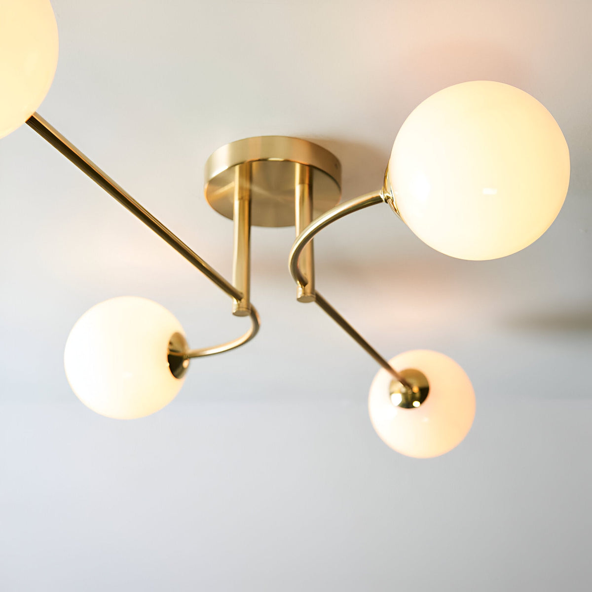 Endon Sinclair 4 light semi-flush ceiling light in brushed brass with four arms holding illuminated white glass globe shades beneath a round central plate.