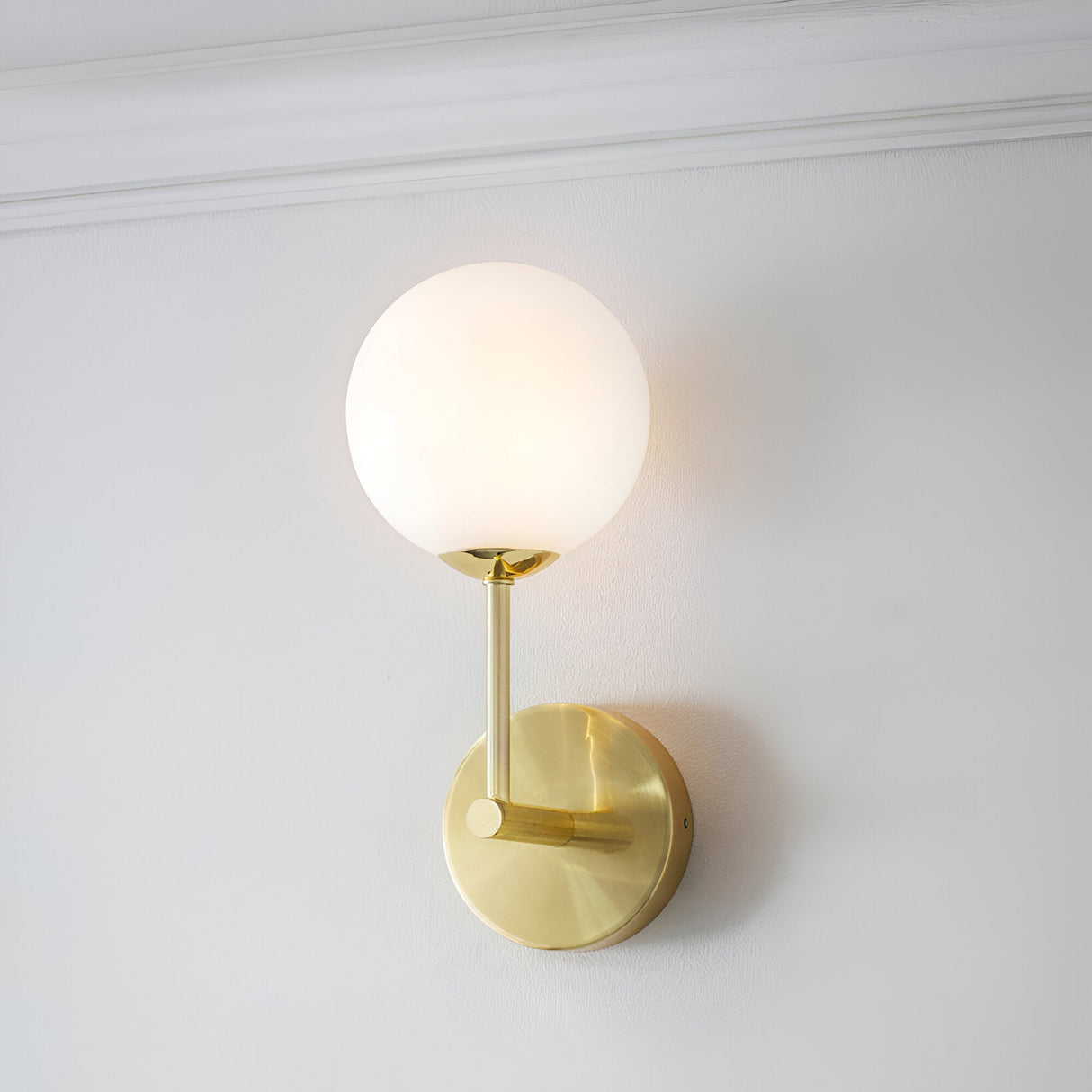 Endon Sinclair wall light with a single opal glass globe on a slim brushed brass stem and round backplate, mounted on a white wall below cornice moulding.