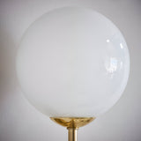 Endon Sinclair wall light with a large gloss opal blown glass globe shade on a brushed brass stem, shown against a plain white wall.