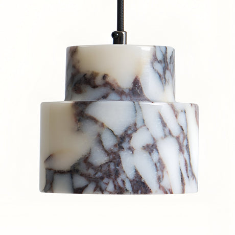 A close-up of the Valmere 1 Light Veined Marble Single Pendant Light in white and black, featuring a cylindrical, tiered white veined marble shade suspended by a black cord against a plain background.