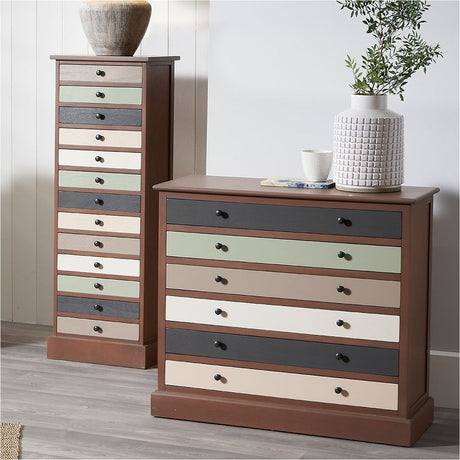 Tall Loft chest of drawers with 13 multicoloured drawer fronts in sage, grey and cream tones, dark wood frame with black knobs, shown beside a matching wide chest in a bedroom setting.