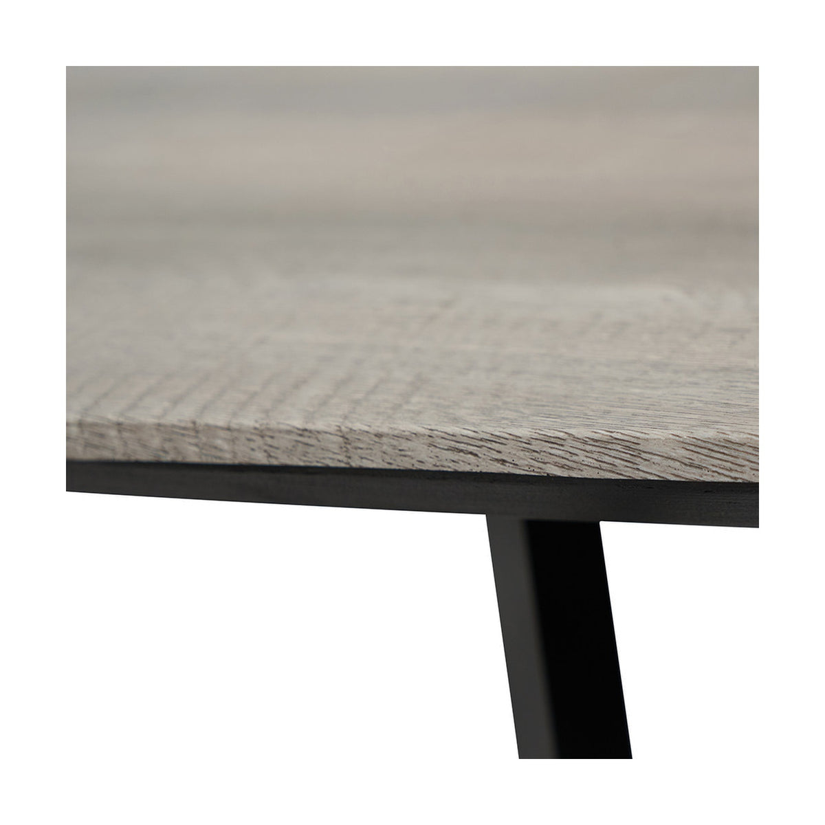 Close-up of the Ukiah dining table's grey oak veneer top edge with visible wood grain, set on a black iron frame and angled leg.