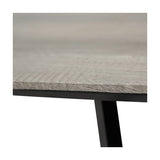 Close-up of the Ukiah dining table's grey oak veneer top edge with visible wood grain, set on a black iron frame and angled leg.