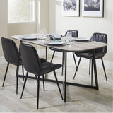 Ukiah Grey Oak Veneer & Black Iron Dining Table set for four with black upholstered chairs, shown in a dining room with framed wall art.