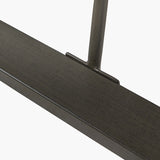 Close-up of the Marca dining table's black iron leg joint against a sand wash acacia wood tabletop edge, shown on a plain white background.