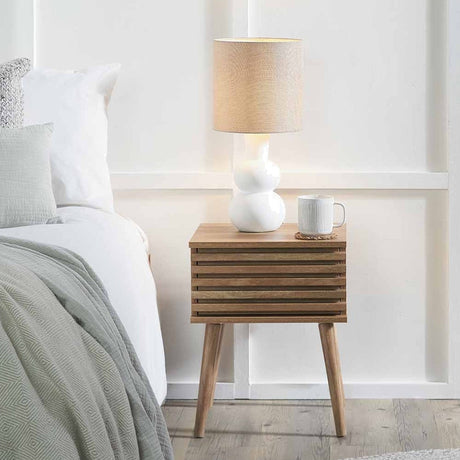 Larvik Eucalyptus Wood 1 Drawer Unit in natural finish with slatted front and tapered legs, styled as a bedside table beside a bed with lamp and mug on top.