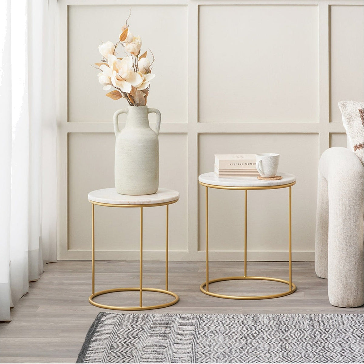 Milly Set of 2 White Marble & Gold Iron Side Tables, 47cm round tables with gold metal frames, styled in a living room with a vase, books, and a mug.