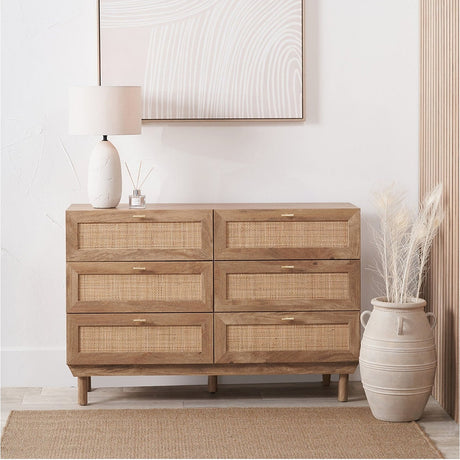 Henrik Rattan 6 Drawer Unit in natural wood with woven rattan drawer fronts and brass handles, shown in a bedroom setting with lamp and decor on top.