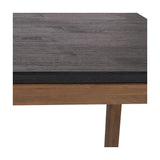 Close-up of the Gio Black & Acacia Dining Table showing a dark wood-grain tabletop edge above a natural acacia frame and tapered leg on a white background.
