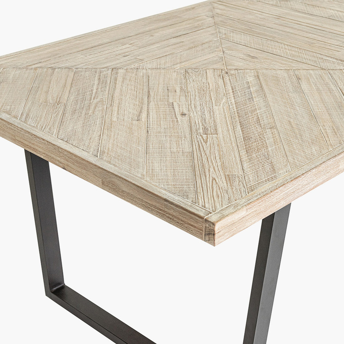 Close-up of the Marca dining table's corner, showing a sand wash acacia wood top with herringbone-style plank pattern and a black metal square-leg frame.