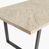 Close-up of the Marca dining table's corner, showing a sand wash acacia wood top with herringbone-style plank pattern and a black metal square-leg frame.