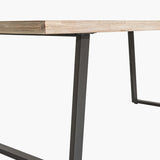Close-up of the Marca dining table's sand wash acacia tabletop edge and angled black metal cross-brace legs, shown against a plain white background.