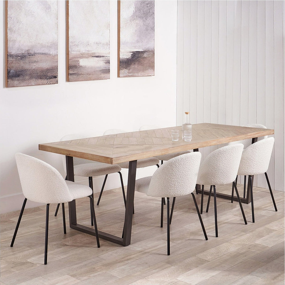 Marca dining table with sand wash acacia wood parquet-style top and black metal sled base, styled in a dining room with white boucle chairs and framed wall art.