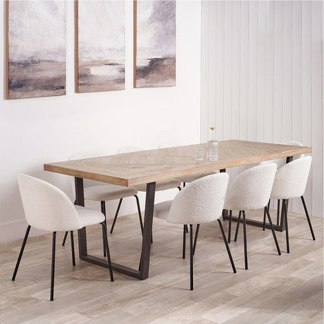 Marca dining table with sand wash acacia wood parquet-style top and black metal sled base, styled in a dining room with white boucle chairs and framed wall art.