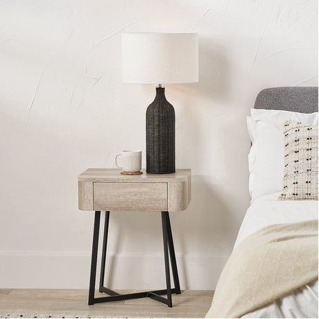 Ukiah grey oak veneer bedside chest with one drawer and black metal angled legs, styled with a table lamp and mug beside a bed.