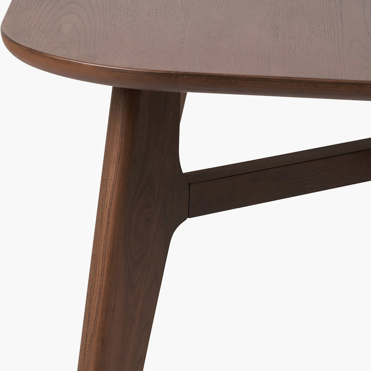 Close-up of the Elias Dark Ash Wood Retro Dining Table showing a rounded tabletop edge, angled tapered leg, and cross-brace joinery in dark ash wood on a plain white background.