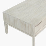 Close-up of the Gio White Sand Acacia 2 Drawer Coffee Table corner, showing white-washed wood grain, tapered leg, and recessed drawer handle on a plain background.