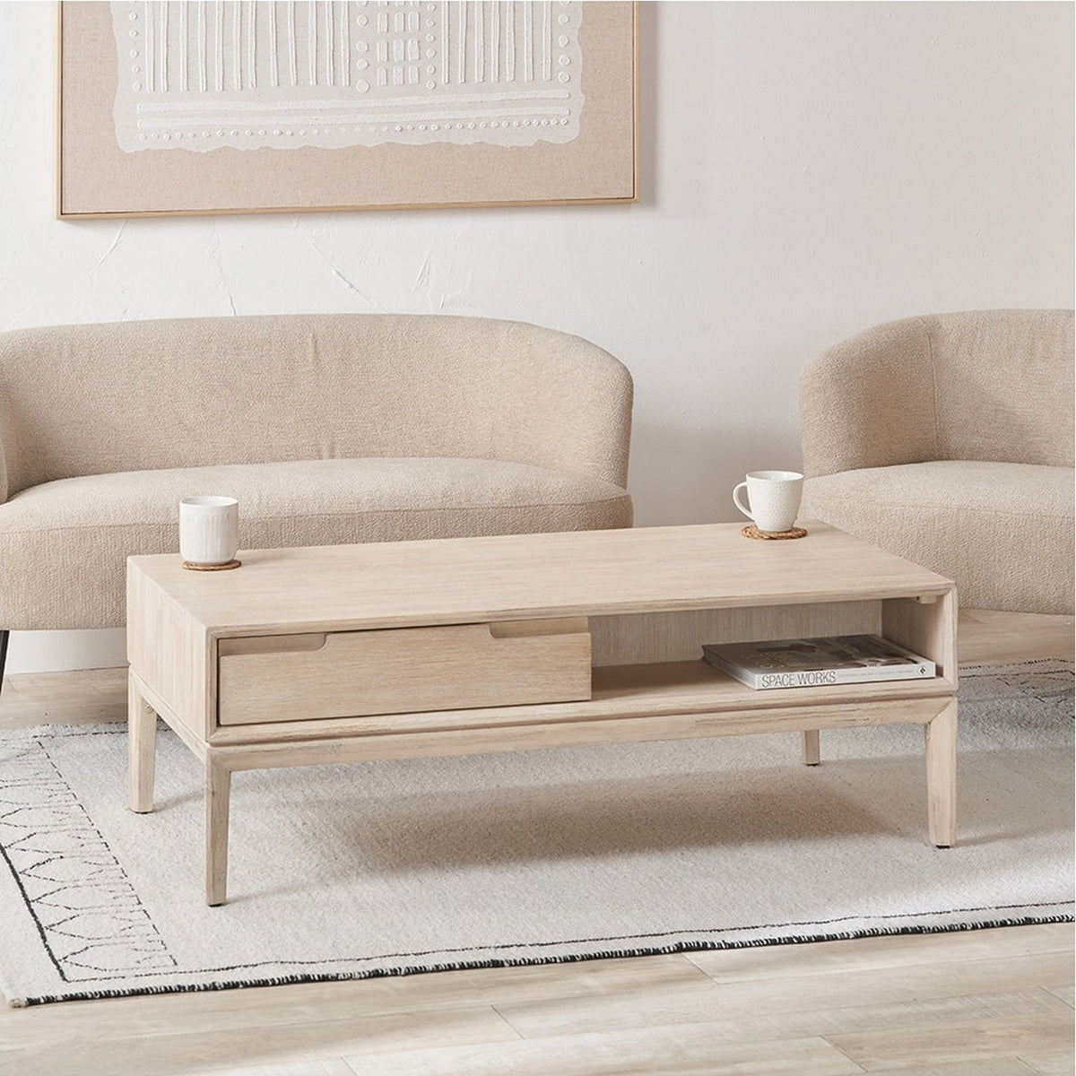 Gio White Sand Acacia 2 Drawer Coffee Table with wooden top, one drawer and open shelf, shown in a living room beside beige sofas on a light rug.
