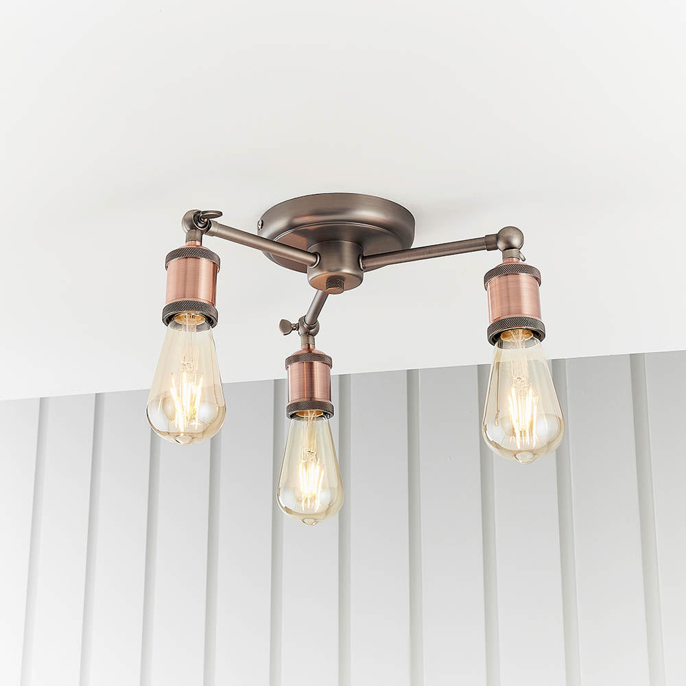 Brackley 3-light semi-flush ceiling light in pewter and copper, three angled arms with copper holders and exposed E27 bulbs, mounted on a white ceiling.