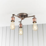 Brackley 3-light semi-flush ceiling light in pewter and copper, three angled arms with copper holders and exposed E27 bulbs, mounted on a white ceiling.