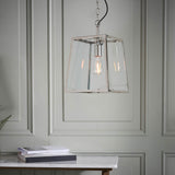 Brenton Lantern Pendant in nickel with clear glass panels and exposed filament bulb, hanging above a marble console table in a panelled room.