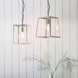 Brenton Lantern Pendant in nickel, box-frame design with clear glass panels and exposed filament bulb, shown in pairs against a white panelled wall.