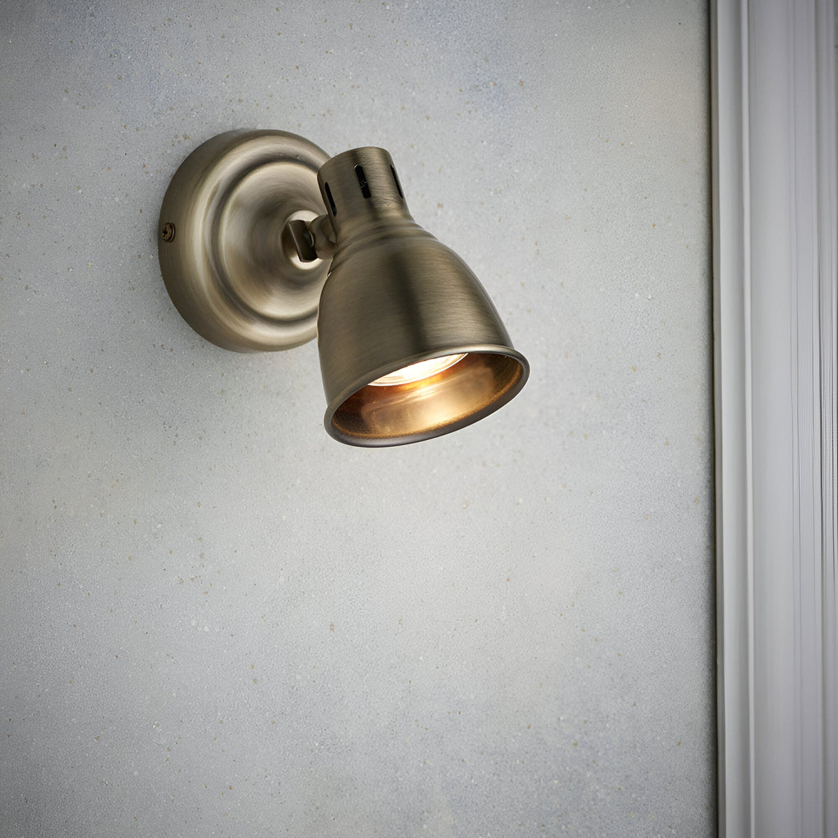 Endon Daneford single spotlight in antique brass with adjustable domed head, mounted on a light wall beside white trim.