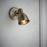 Endon Daneford single spotlight in antique brass with adjustable domed head, mounted on a light wall beside white trim.