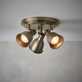 Endon Daneford 3 light round ceiling spotlight in antique brass with three independently adjustable steel heads, shown lit against a plain grey background.
