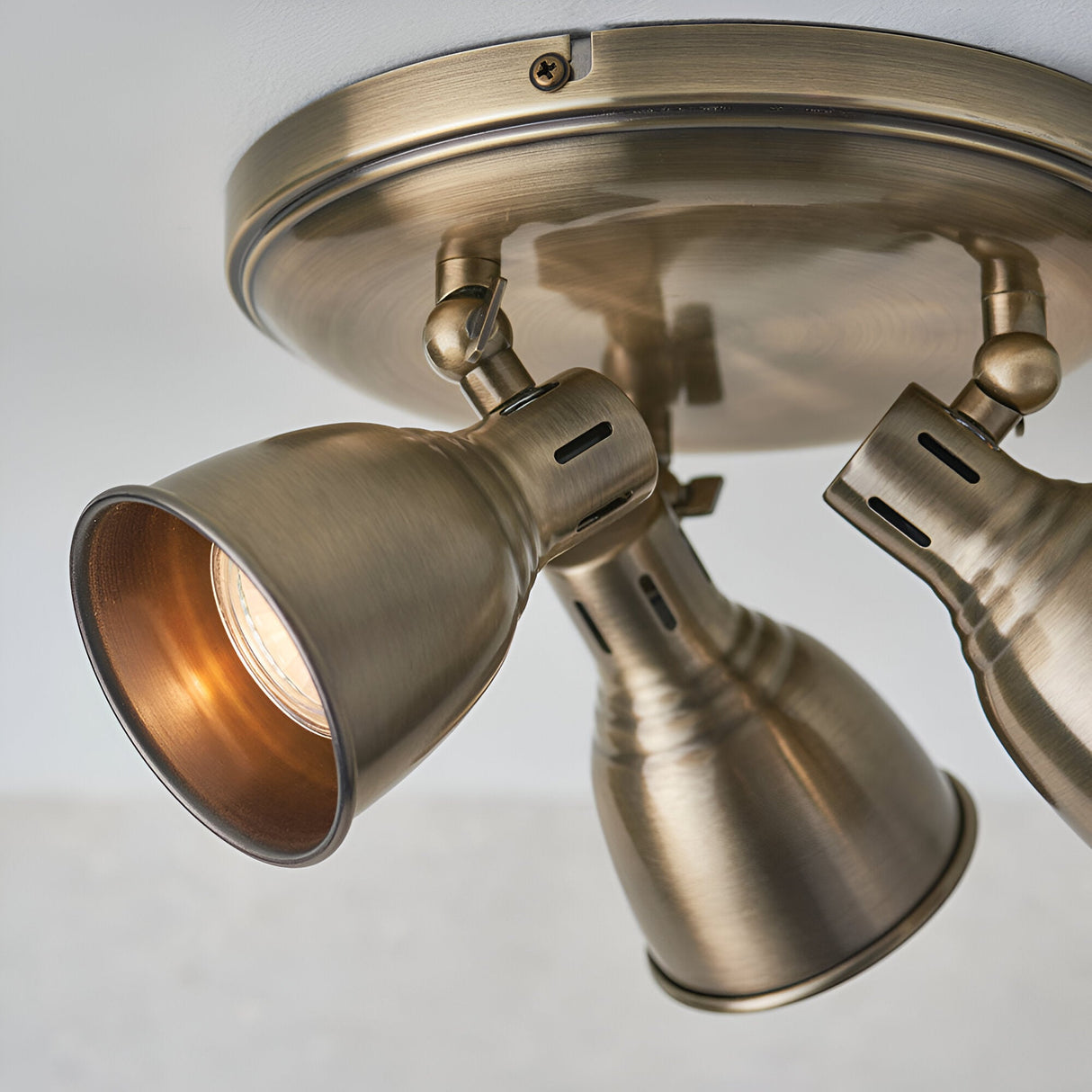 Close-up of the Endon Daneford 3 light round spotlight in antique brass, showing adjustable steel heads on a circular ceiling plate.