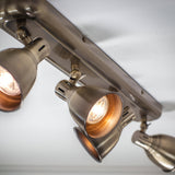 Close-up of Endon Daneford 4 Light Spotlight in antique brass, showing adjustable steel heads on a linear ceiling plate with lit bulbs.