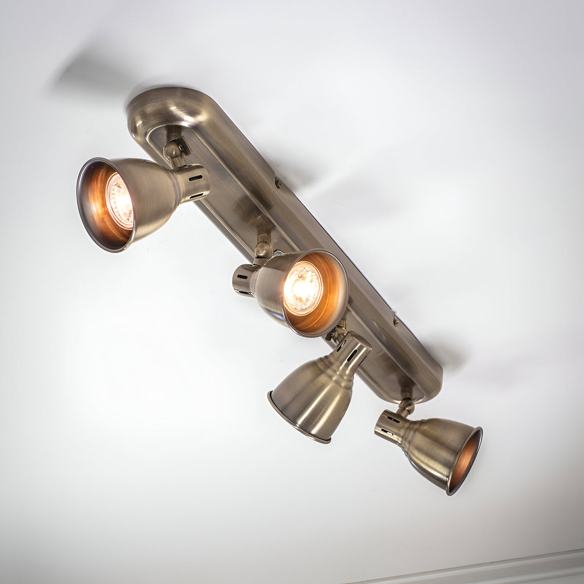 Endon Daneford 4 light spotlight in antique brass, ceiling-mounted with four adjustable heads on a linear plate, two lit, viewed from below.