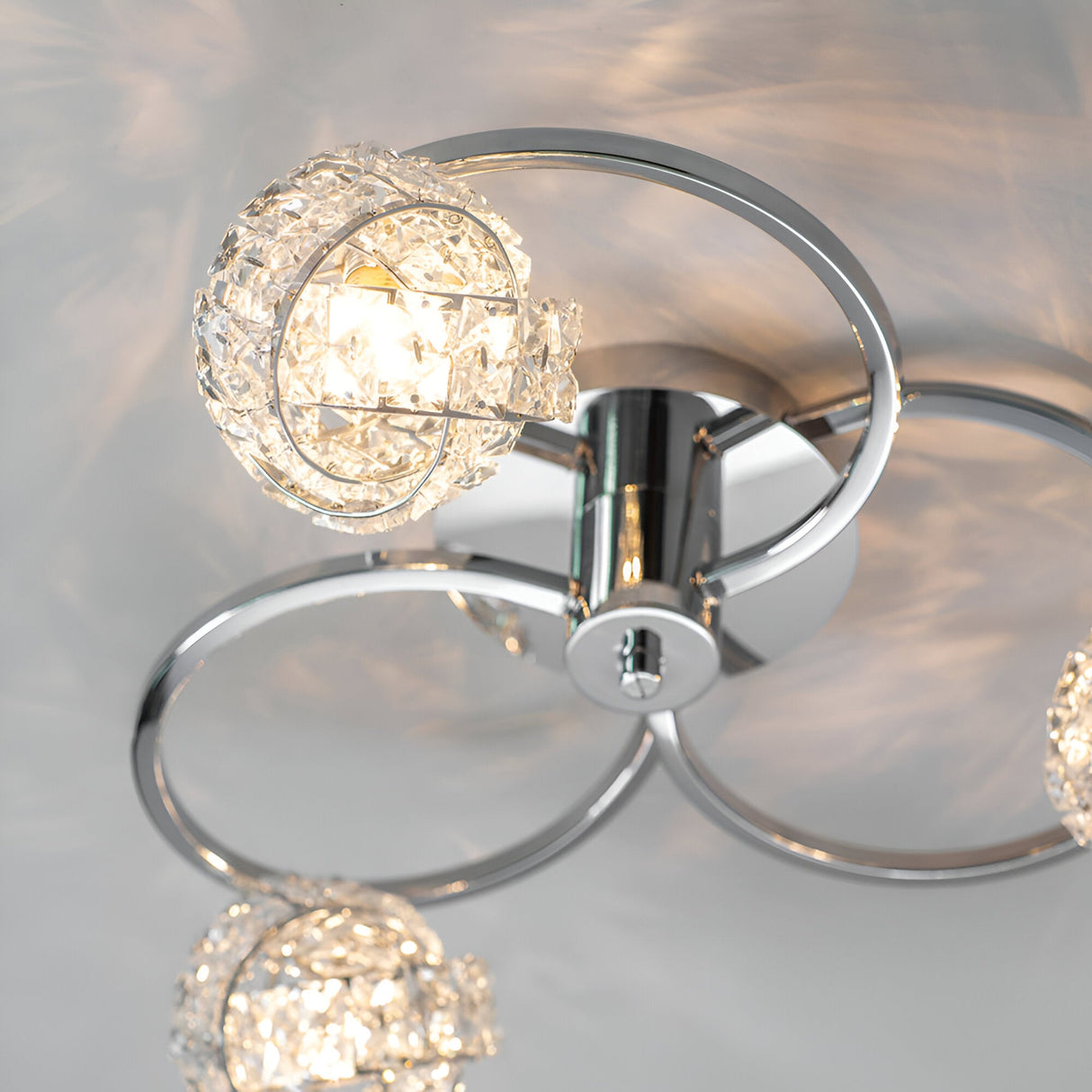 Endon Seraphine 3 light semi-flush ceiling light in polished chrome, with faceted crystal globe shades on circular ring arms, shown lit from below.