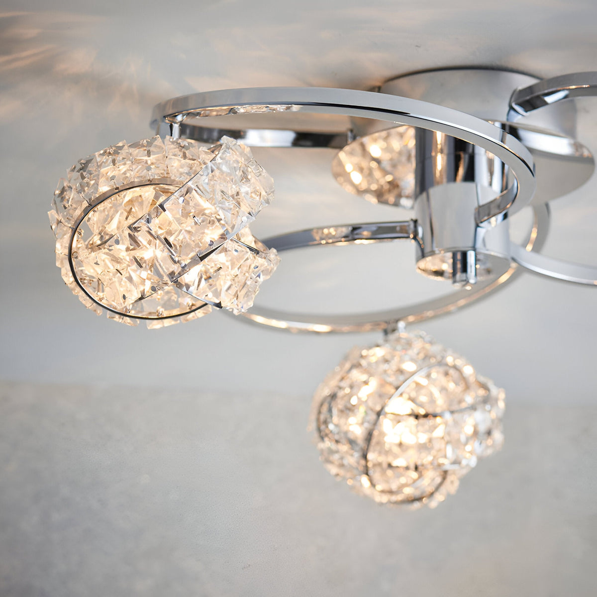 Endon Seraphine 3 light semi-flush ceiling light in polished chrome with faceted crystal globe shades, shown illuminated close to the ceiling.