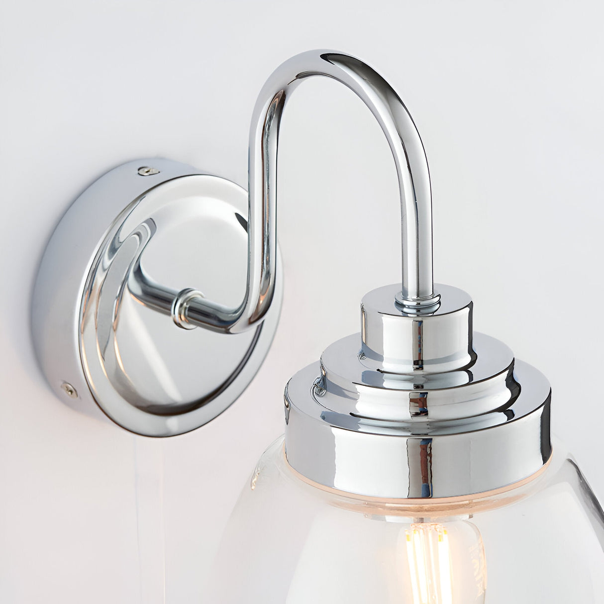 Close-up of Endon Bramworth bathroom wall light showing polished chrome wall plate, curved arm, and clear glass shade fitting with E14 bulb.