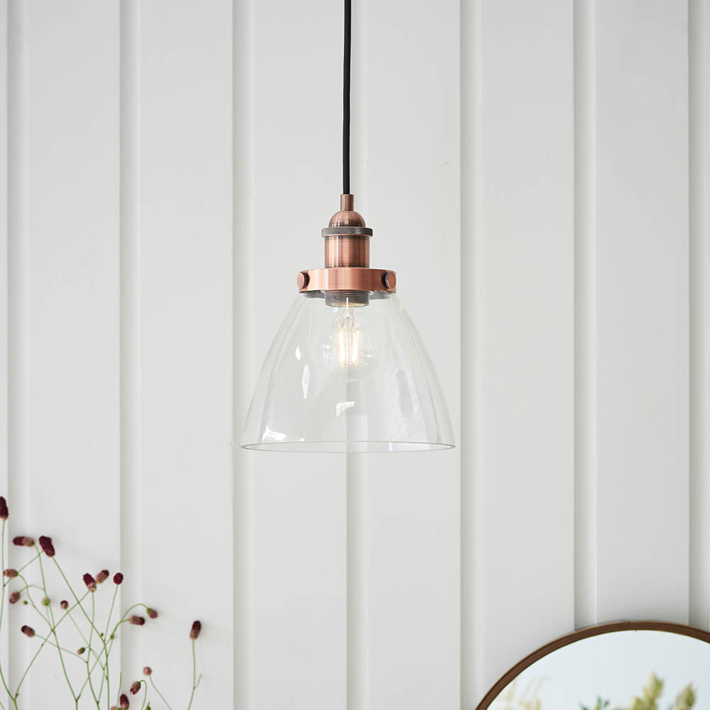 Endon Wentworth industrial pendant light in copper with a clear glass dome shade, knurled lamp holder and black fabric flex, hung against white panelling.