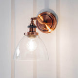 Endon Wentworth wall light in copper with adjustable knuckle, knurled lamp holder and clear glass dome shade, mounted on a white panelled wall.