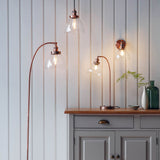 Endon Wentworth wall light in copper with clear glass shade and lit filament bulb, shown beside matching pendant and table lights above a grey sideboard.