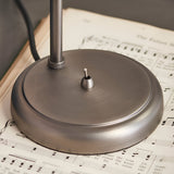 Close-up of the Brackley Table Lamp's round metal base in silver, showing the knurled adjustable joint and on/off toggle switch, set on sheet music.