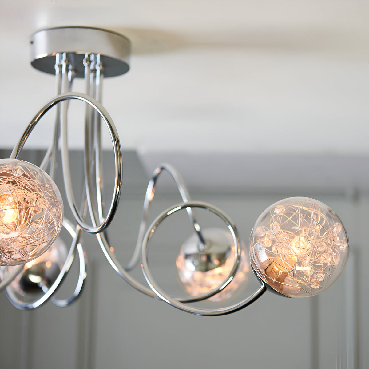 Close-up of Endon Sabine 6 light semi-flush ceiling light in chrome, showing looped steel arms and clear glass globes with inner wire detail.