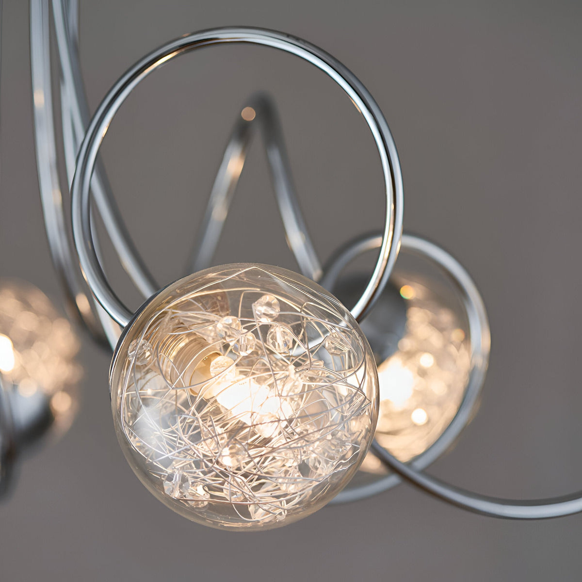 Close-up of Endon Sabine semi-flush ceiling light showing a glass globe filled with fine wires and crystals, framed by looping chrome steel arms.