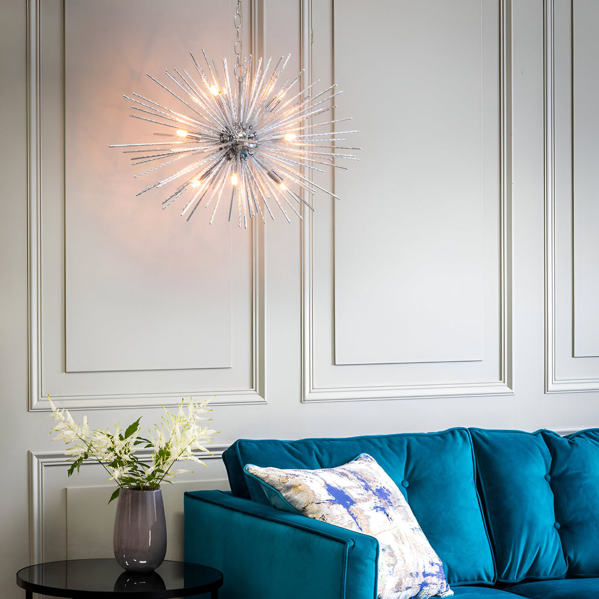 Endon Caldleigh 9 light starburst pendant in polished chrome with radiating rods and G9 lamps, above a teal velvet sofa and panelled wall.