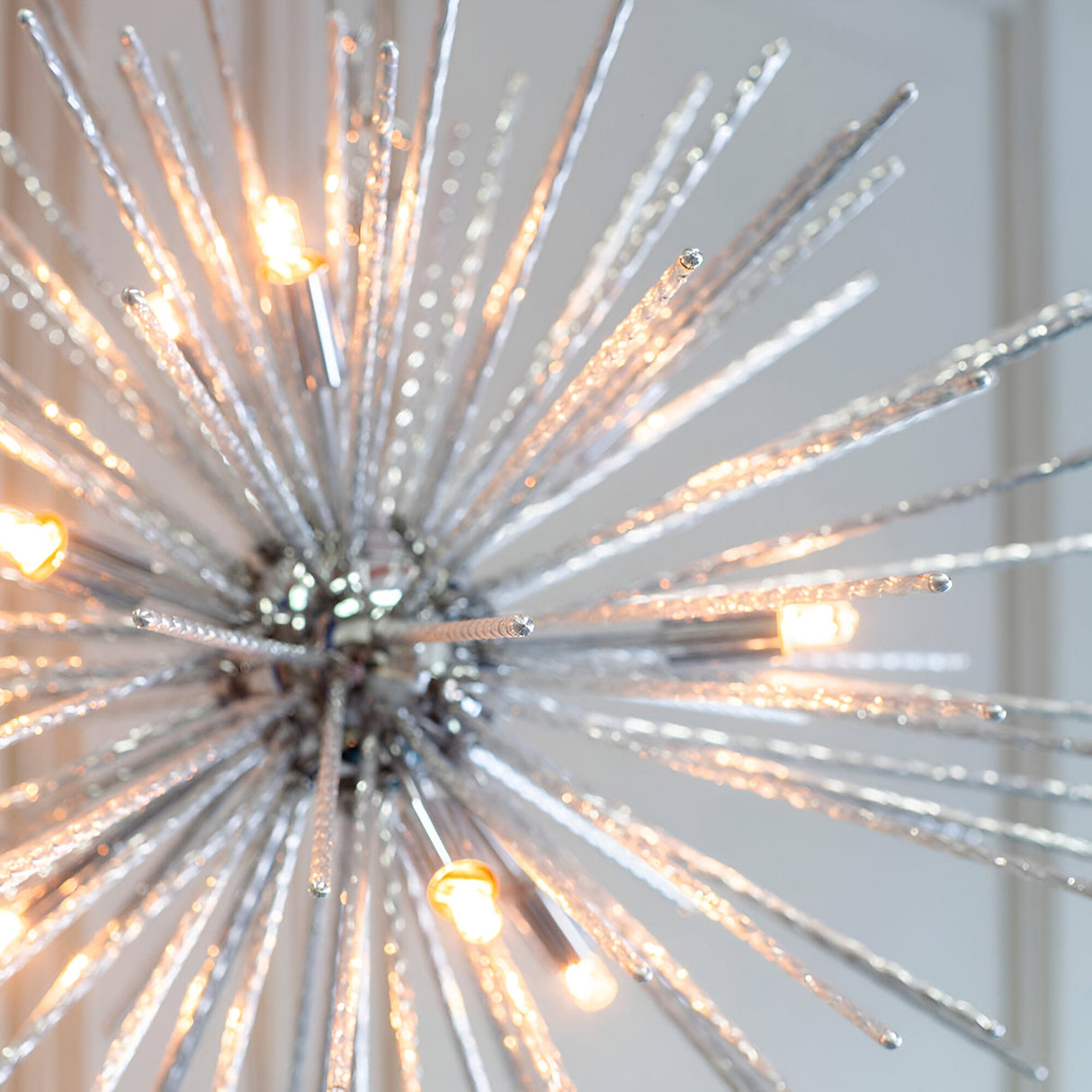 Close-up of Endon Caldleigh 9 light pendant with textured polished chrome rods fanning out in a starburst around lit G9 lamps.