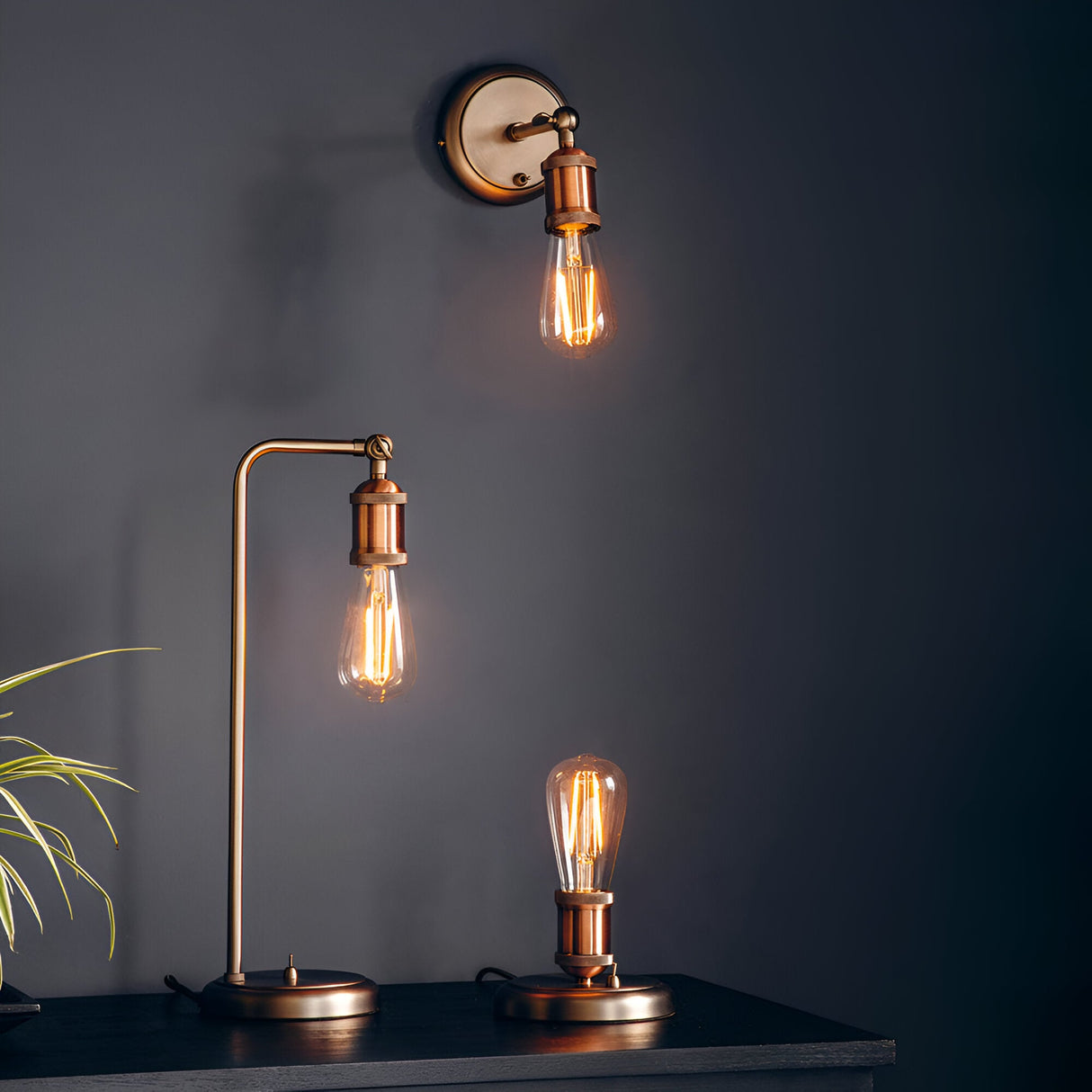 Endon Brackley table lamp in aged pewter and copper with exposed filament bulb, shown beside a matching wall light and small base lamp against a dark wall.