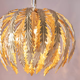 Endon Colette 3 light pendant with layered gold leaf fronds fanning over illuminated bulbs, suspended from a chain against a soft neutral background.