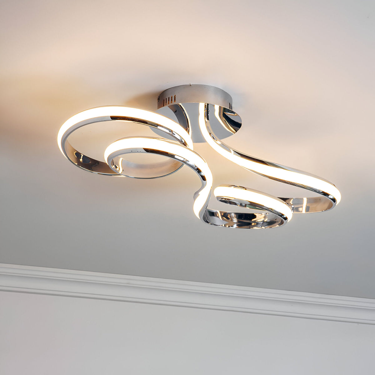 Endon Neve semi-flush ceiling light with swirling looped LED bands in polished chrome, mounted to a ceiling above white cornice.
